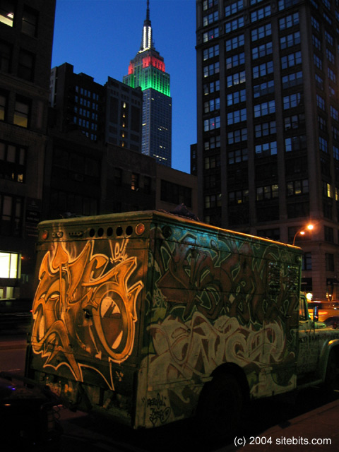 Empire State Building at night with a funky vehicle in front.